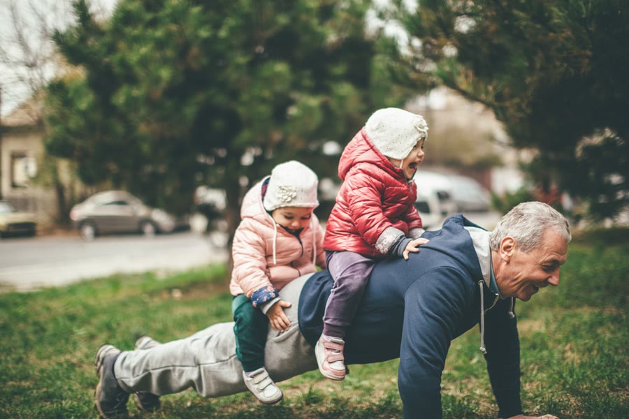 Grandfather playing on the grass with his two grandchildren on his back
