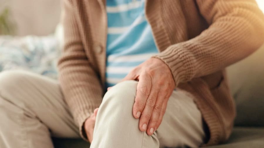 Older adult seated at home holding an aching knee
